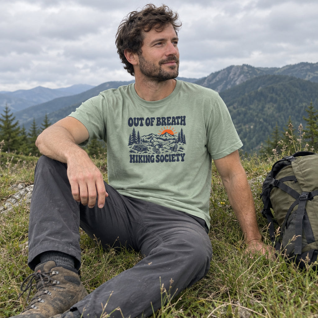 Man wearing the Out of Breath Hiking Society Flat Out T-Shirt sitting in mountain grass next to a backpack