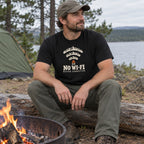 Man wearing the No Wi-Fi, Better Connection T-shirt sitting by a campfire ring at a campsite